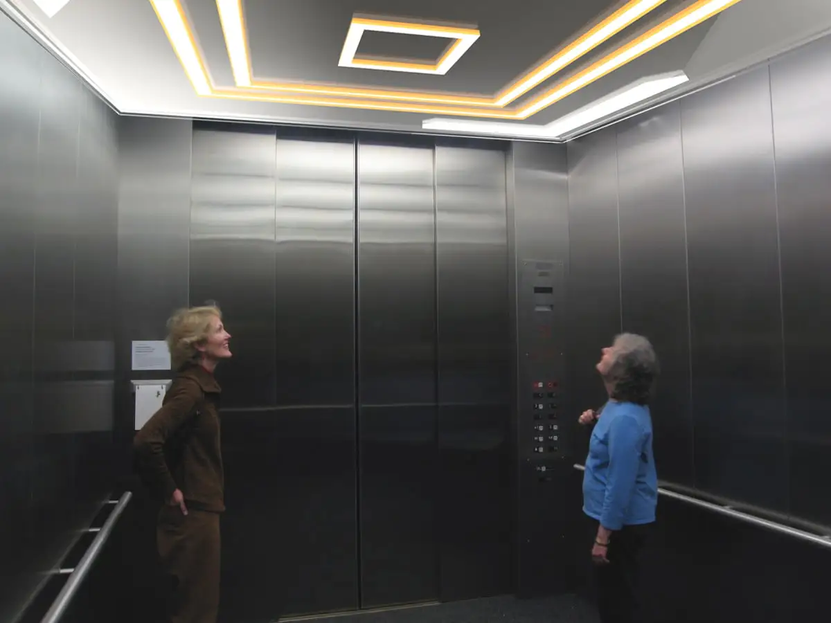 Elevator Cab Lighting Ideas illustrated with two women standing in a well lit elevator - Elevator Cab Lighting Ideas: Enhancing Ambiance and Functionality - Vorlane - Vorlane